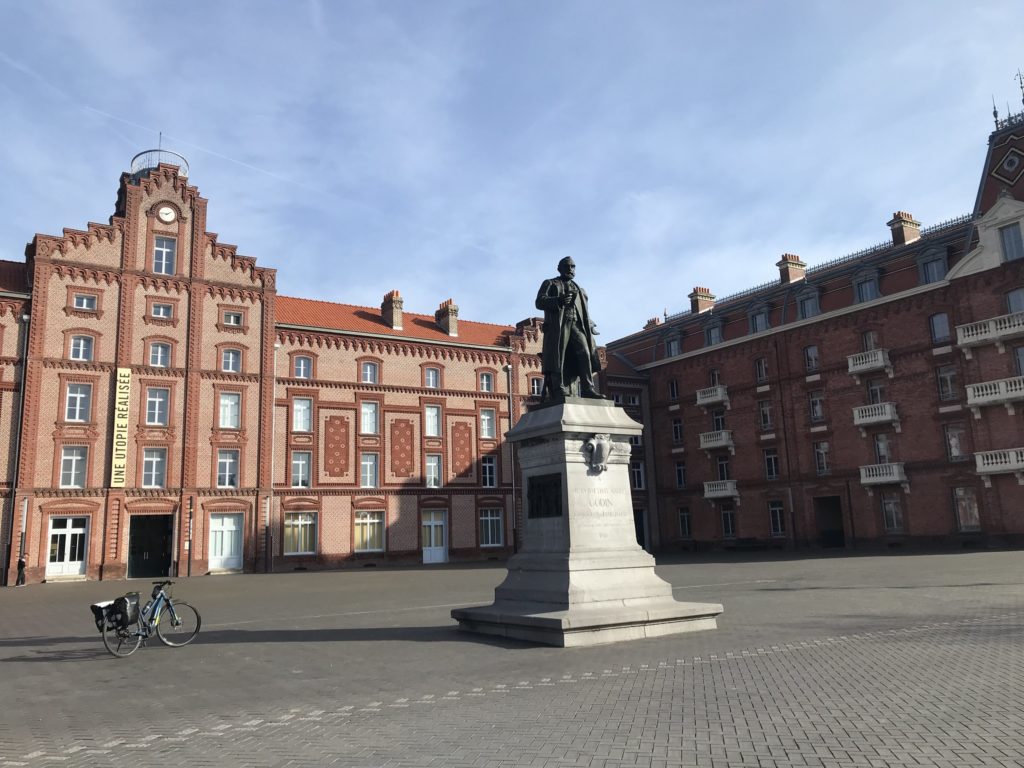 Vélo devant bâtiment en briques routes et statue à droite