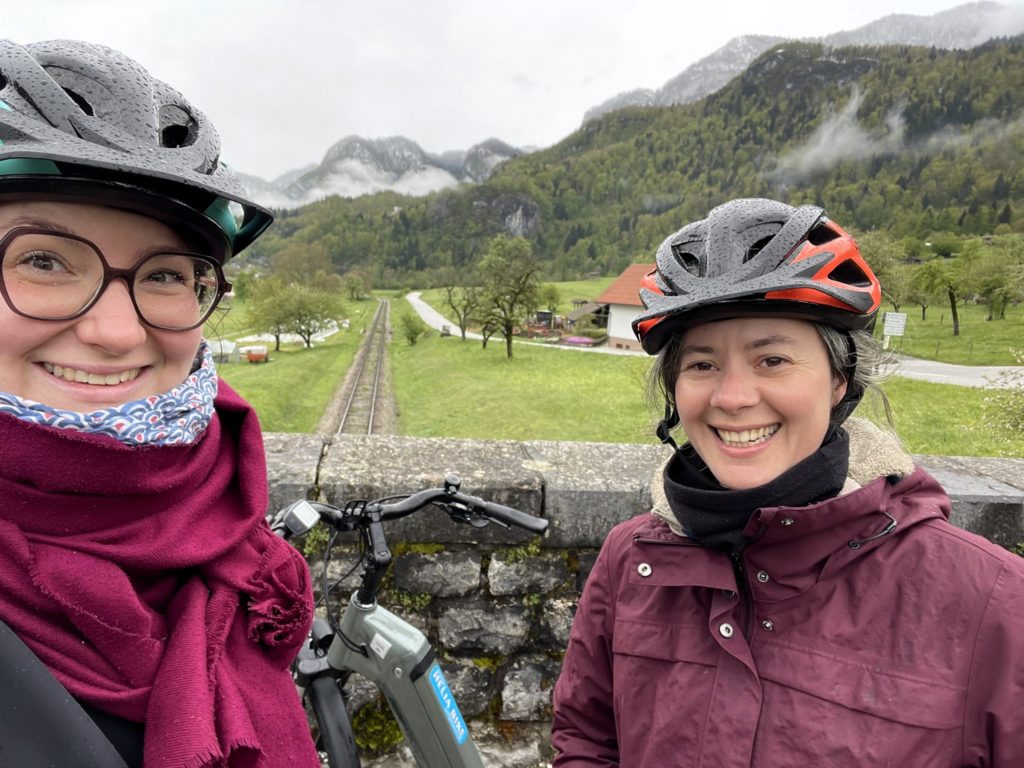 2 cyclistes sourient avec en arrière plan les montagnes enneigées